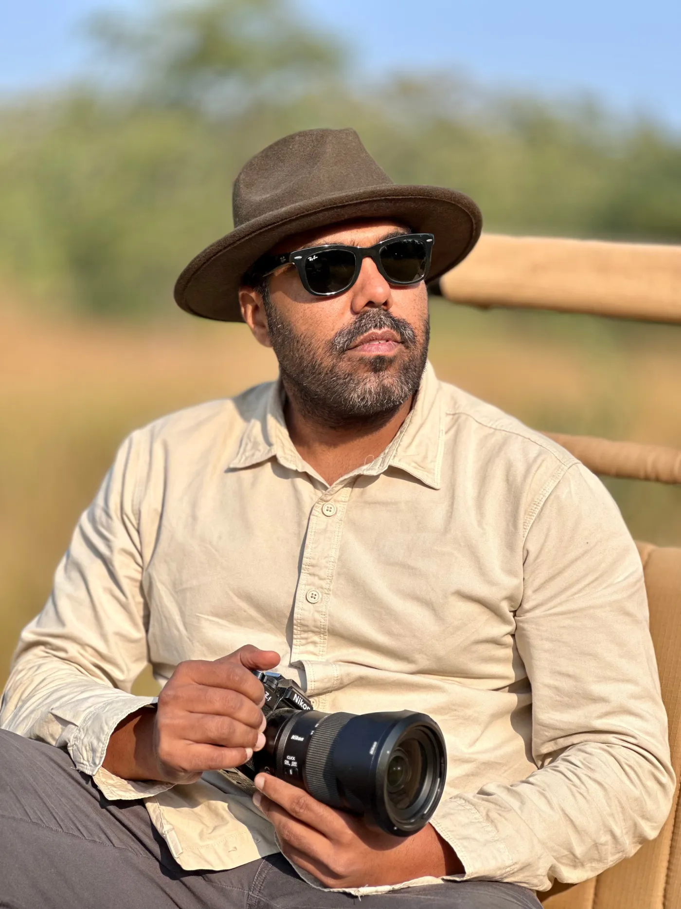Tarun Siwach in the back of an open vehicle in Panna, camera in hand, dry grass behind him